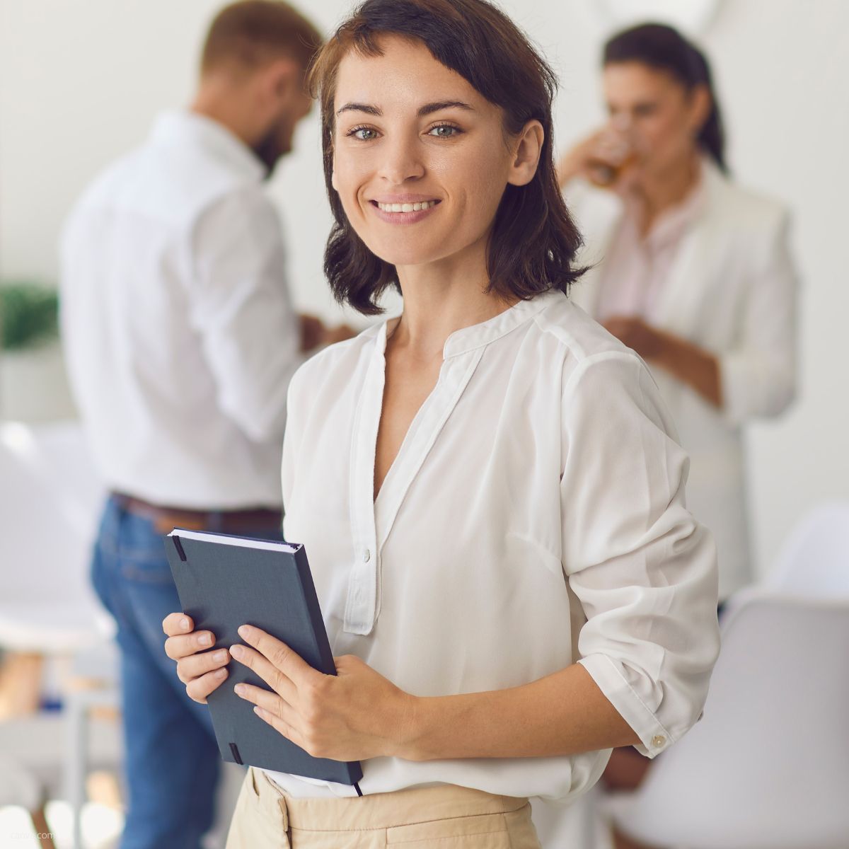 Businessfrau mit Notizbuch in der Hand, stehend vor Kollegen im Hintergrund