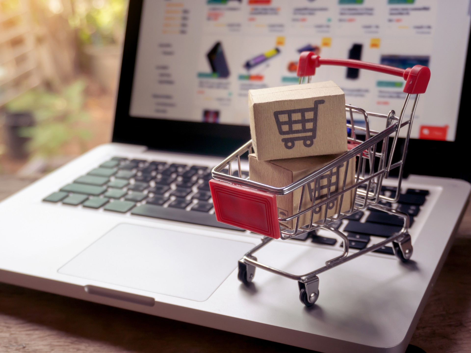 Laptop mit darauf stehendem Einkaufswagen als Symbol für E-Commerce und Online-Shopping